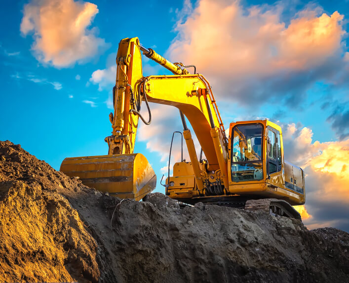 Yellow excavator on a dirt mound at sunset, illustrating why are diesel engines used for heavy equipment due to power and durability.