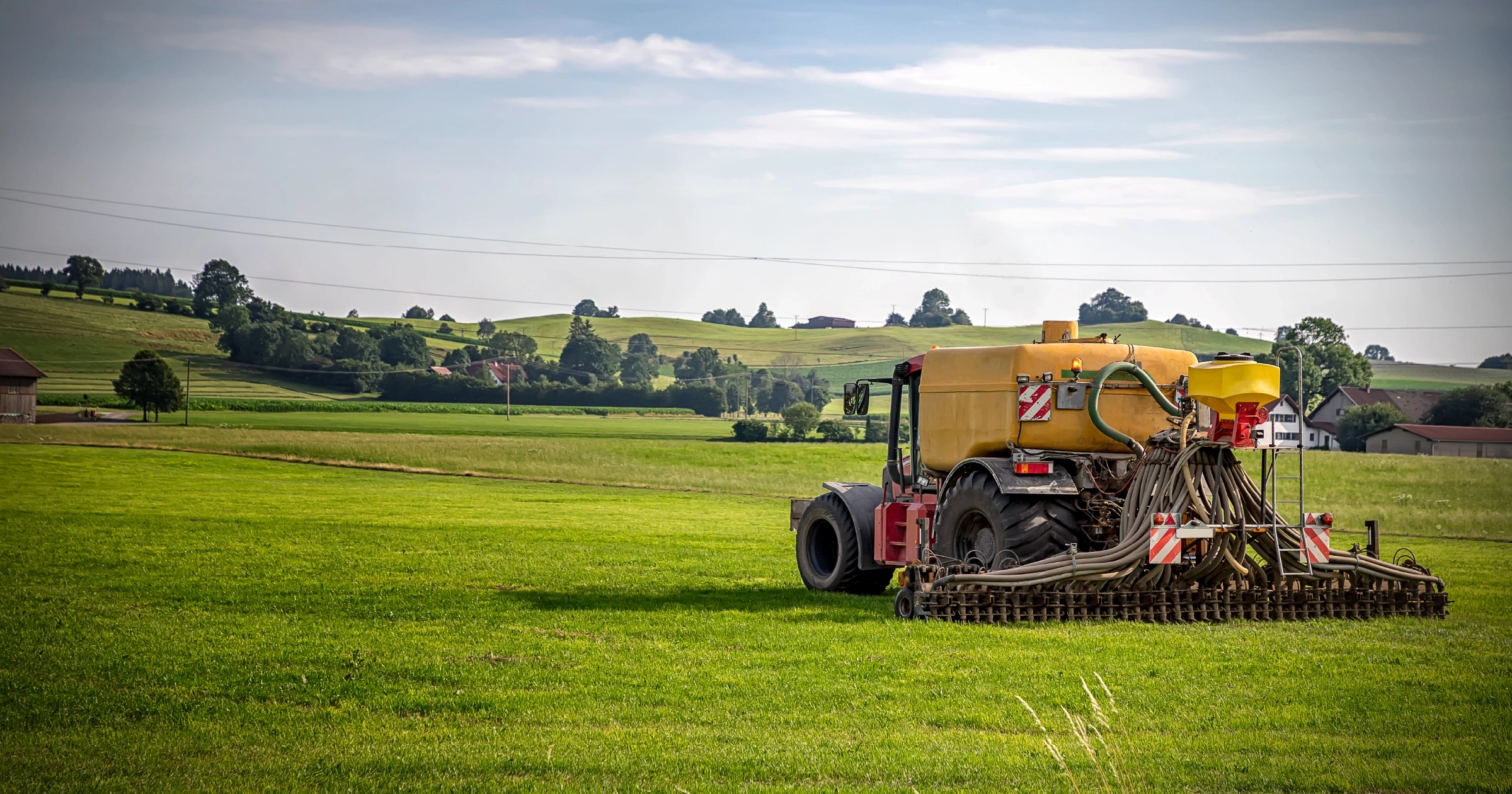RF-Blog-FeatureImage-What-Is-Diesel-Fuel-for-Farm-Use2x 1 - Rhino Fuel A large yellow tractor-mounted sprayer in a green field with rolling hills and farm buildings in the distance